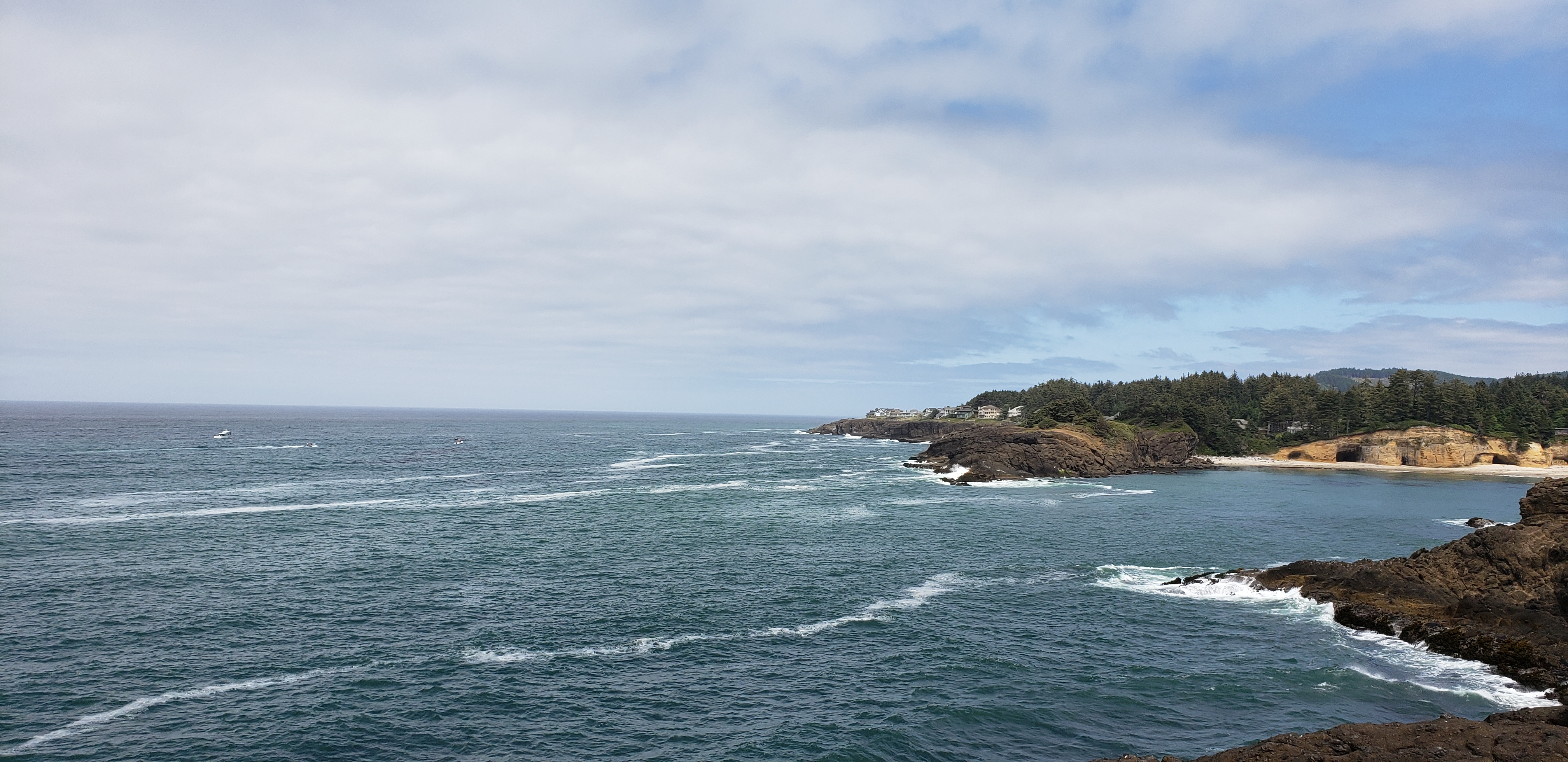 Blue ocean with light whitecap waves beneath overcast sky, rocky shoreline with expensive homes on cliff in distance on right